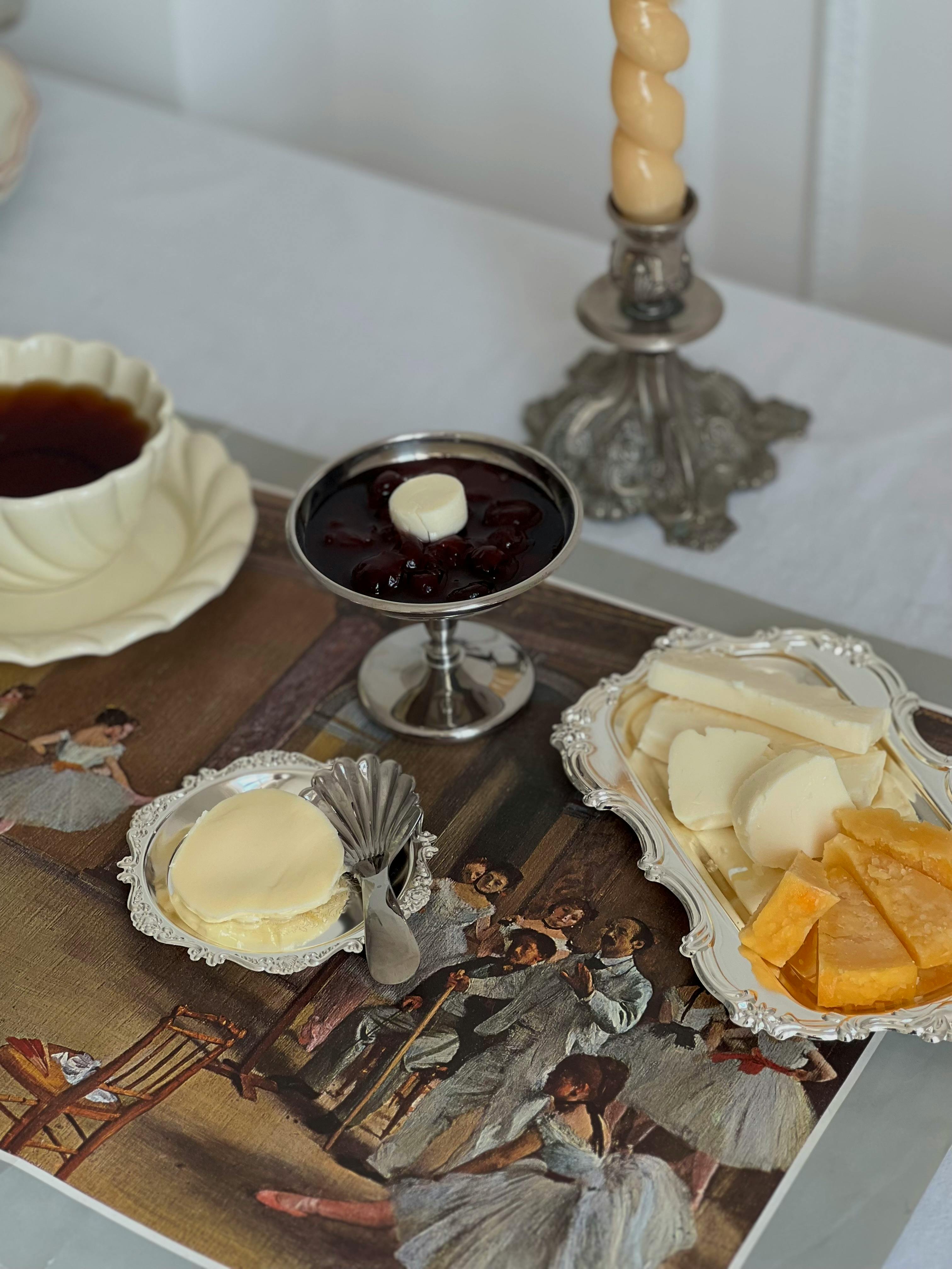 A vintage cheese platter set beside a classic painting and ornate candle holder.