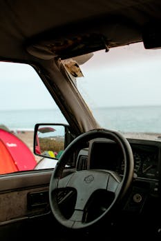 Steering wheel view from a vintage car on a beachside, showcasing travel vibes.