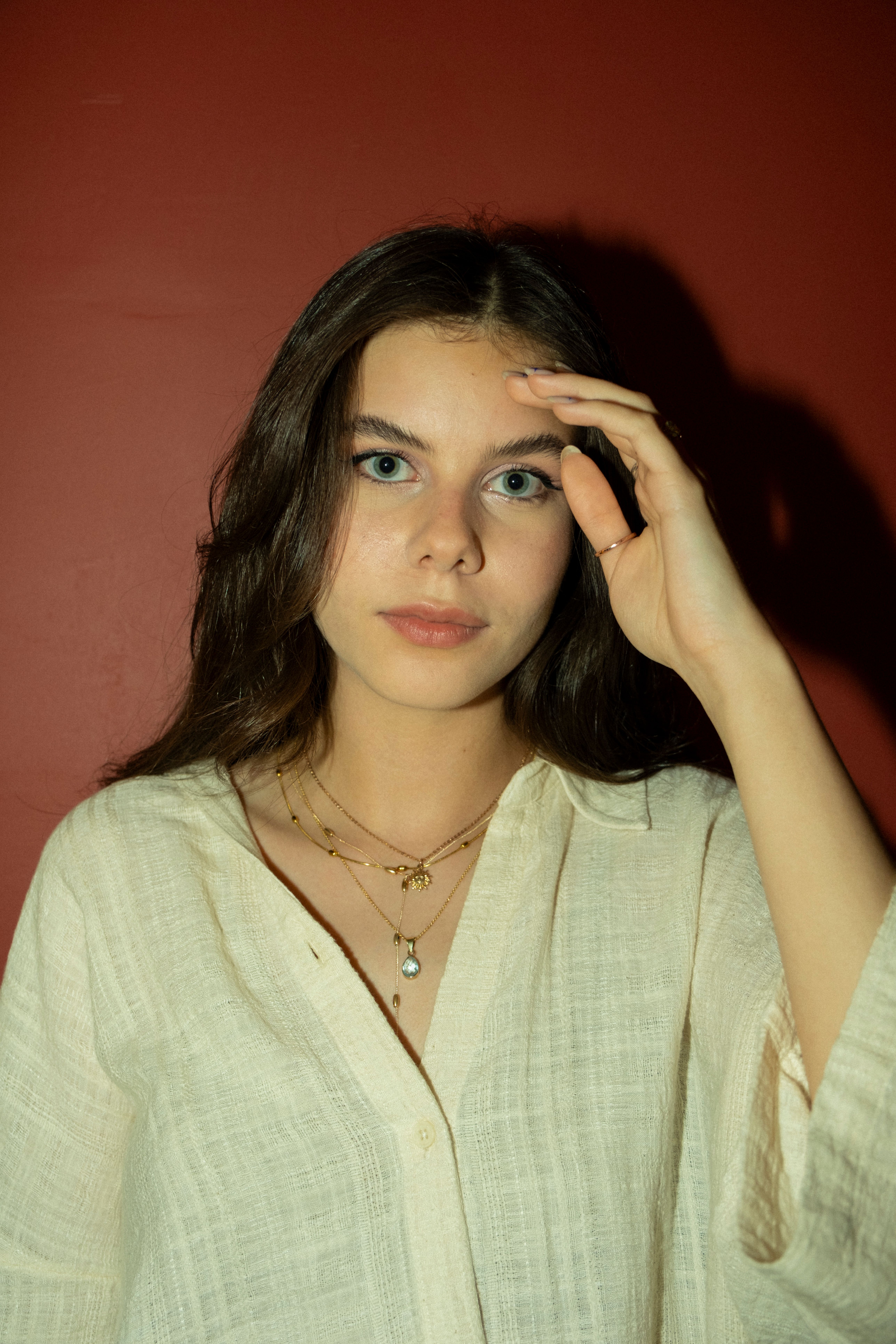Portrait of a young woman with delicate jewelry posing indoors with a neutral expression.