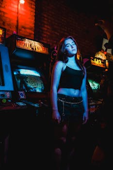 A young woman stands in a neon-lit arcade surrounded by retro gaming machines.