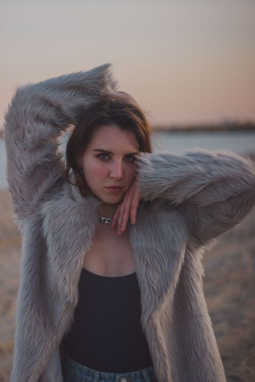 Free Elegant woman posing in a fur coat at sunset near a lake, embodying winter fashion. Stock Photo