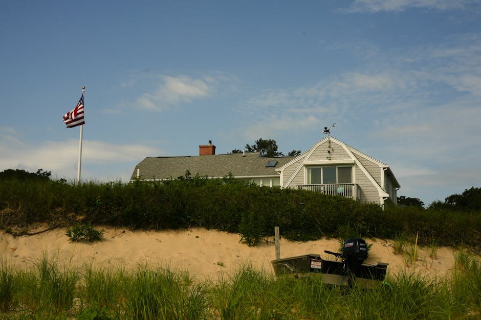 Picturesque Beach House with American Flag A picturesque beach house with an American flag, surrounded by dune grass on a sunny day.