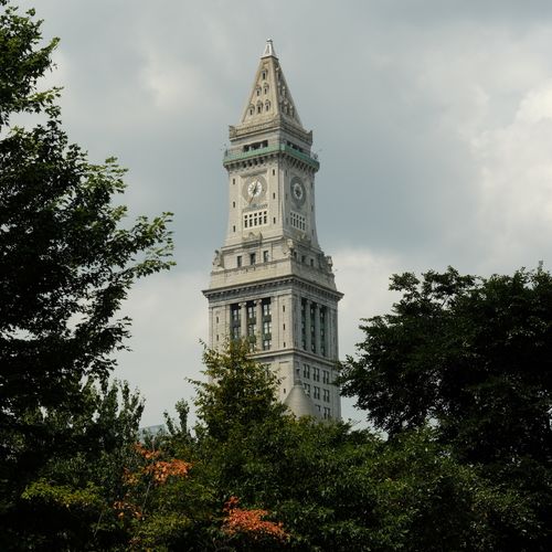 Free A stately clock tower surrounded by lush trees under a cloudy sky, showcasing historic architecture. Stock Photo