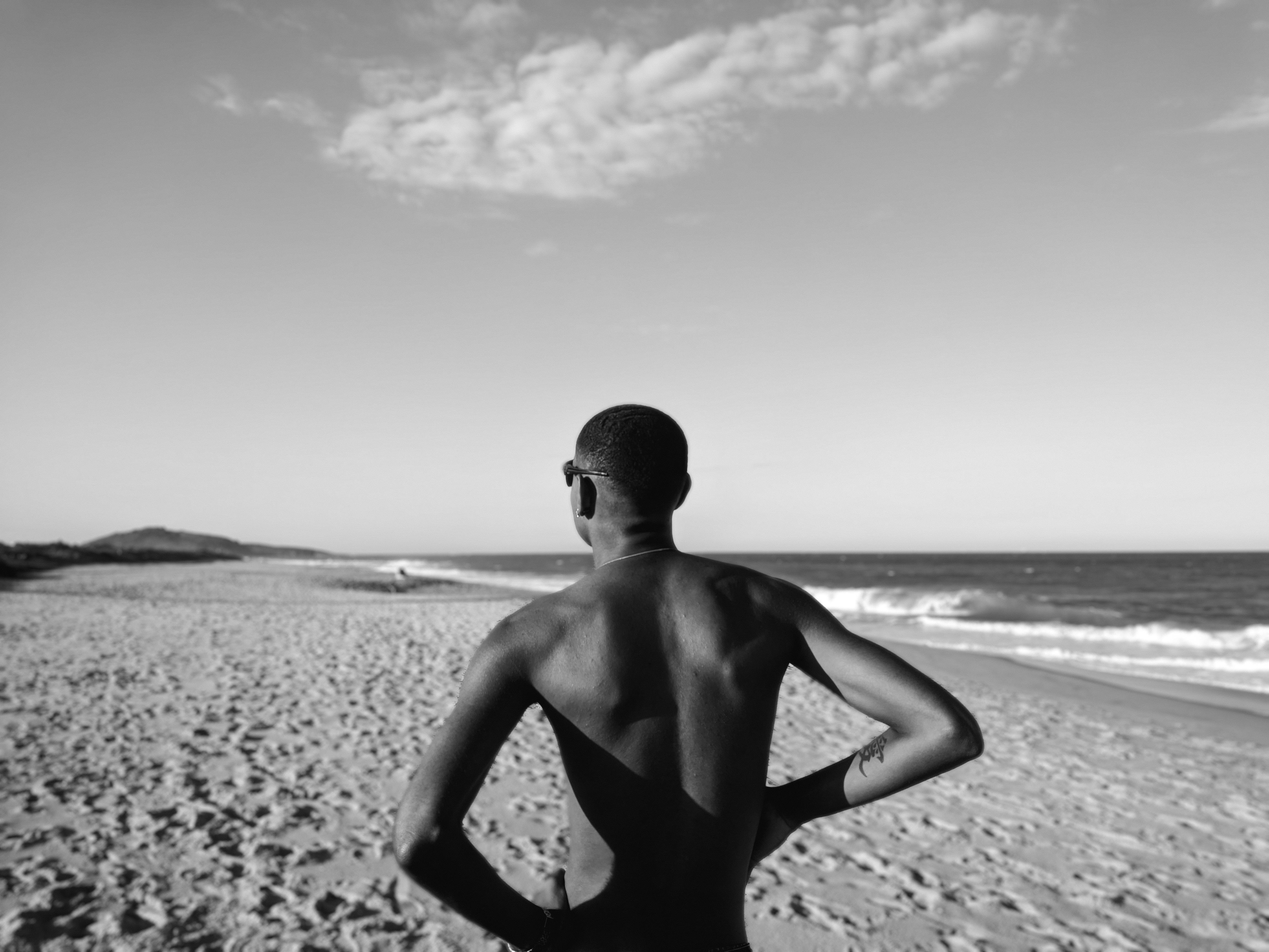 Black and white photo of a man contemplating at a sandy seashore.