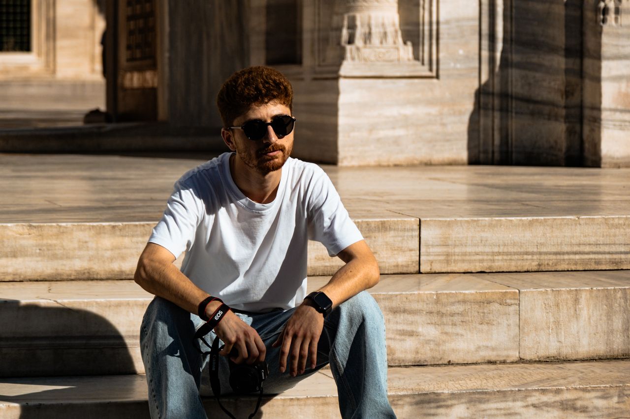 a man in sunglasses sits on marble steps enjoying daylight in a stylis