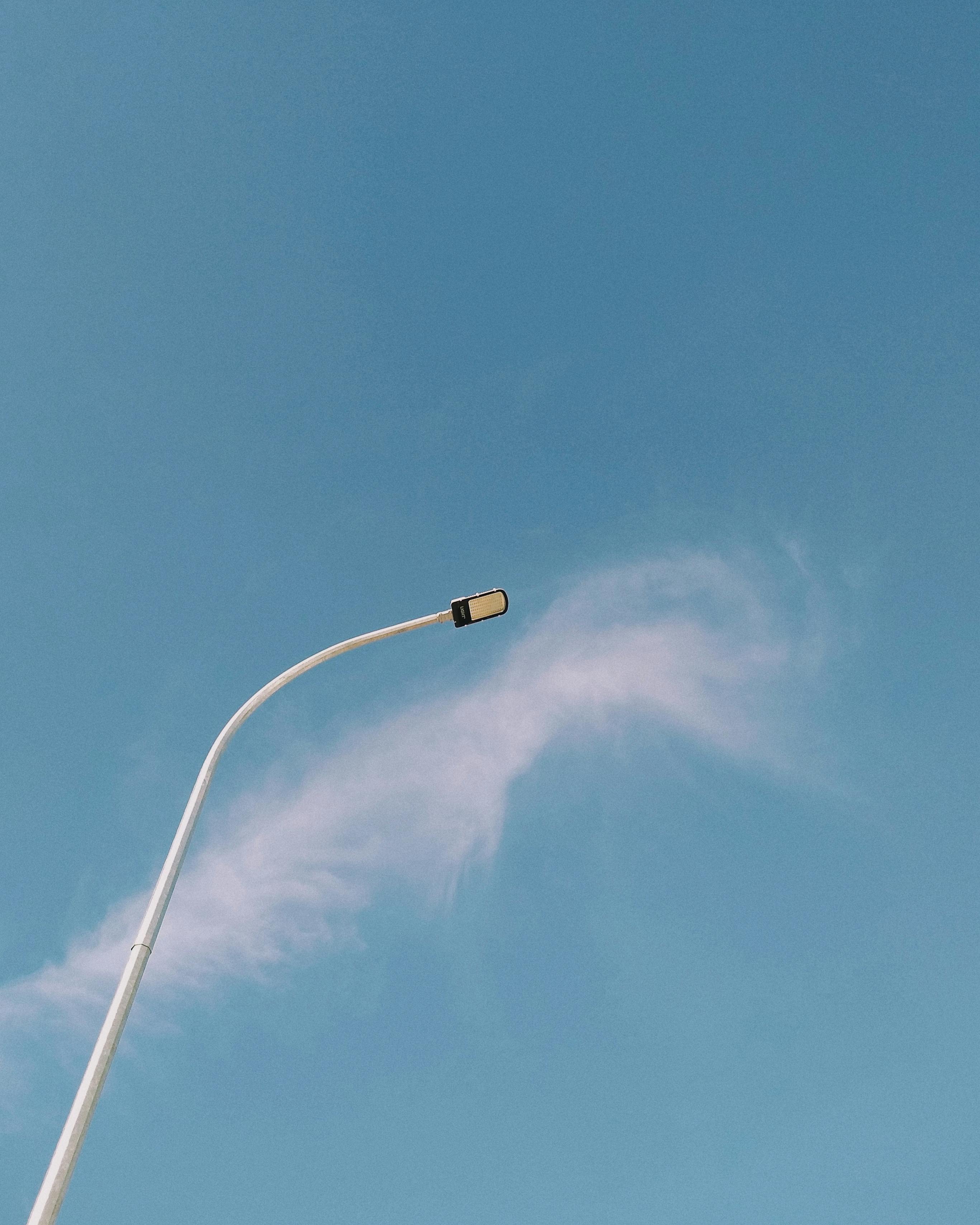 A minimalist street lamp stands tall against a backdrop of clear blue sky with wispy clouds.