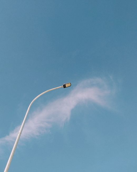 A minimalist street lamp stands tall against a backdrop of clear blue sky with wispy clouds.