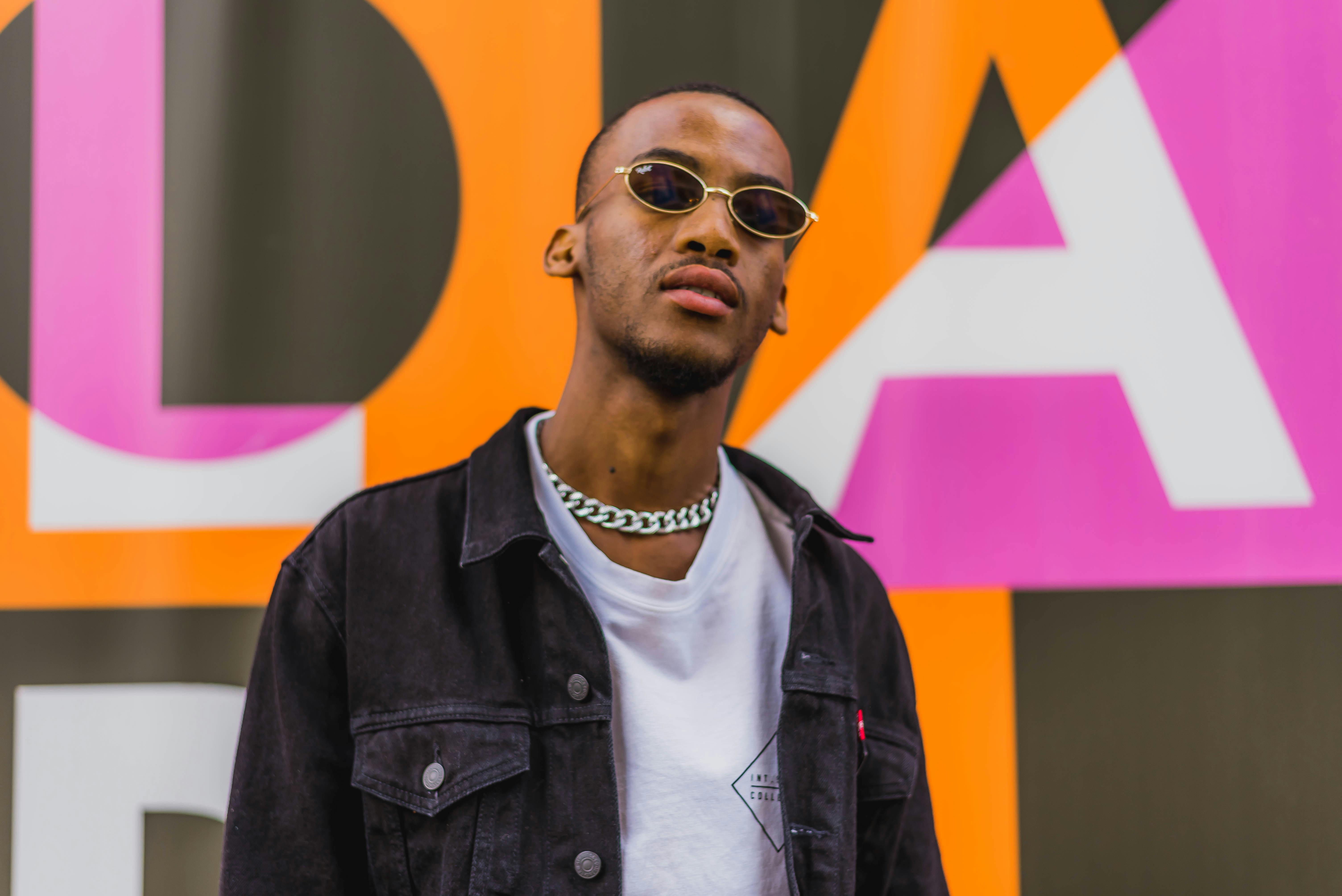 Free Stylish man in sunglasses and chain necklace against colorful urban background. Stock Photo