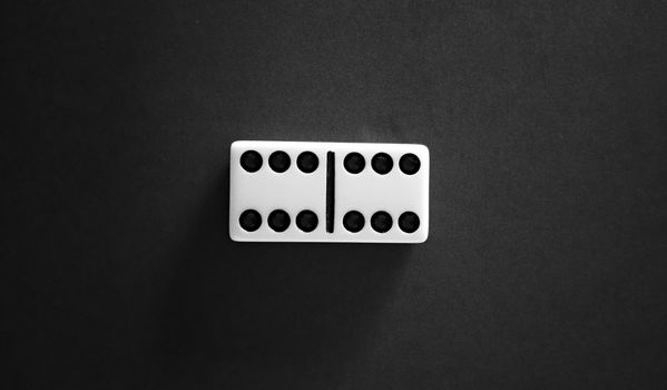 Close-up of a domino tile on a black background, capturing minimalist design in photography.