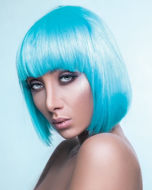 Striking portrait of an adult woman with vibrant blue hair and captivating eyes on a light background.