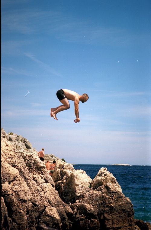 Free A man diving off rocky cliffs into the blue Adriatic Sea near Rovinj, Croatia, capturing the essence of summer adventure. Stock Photo