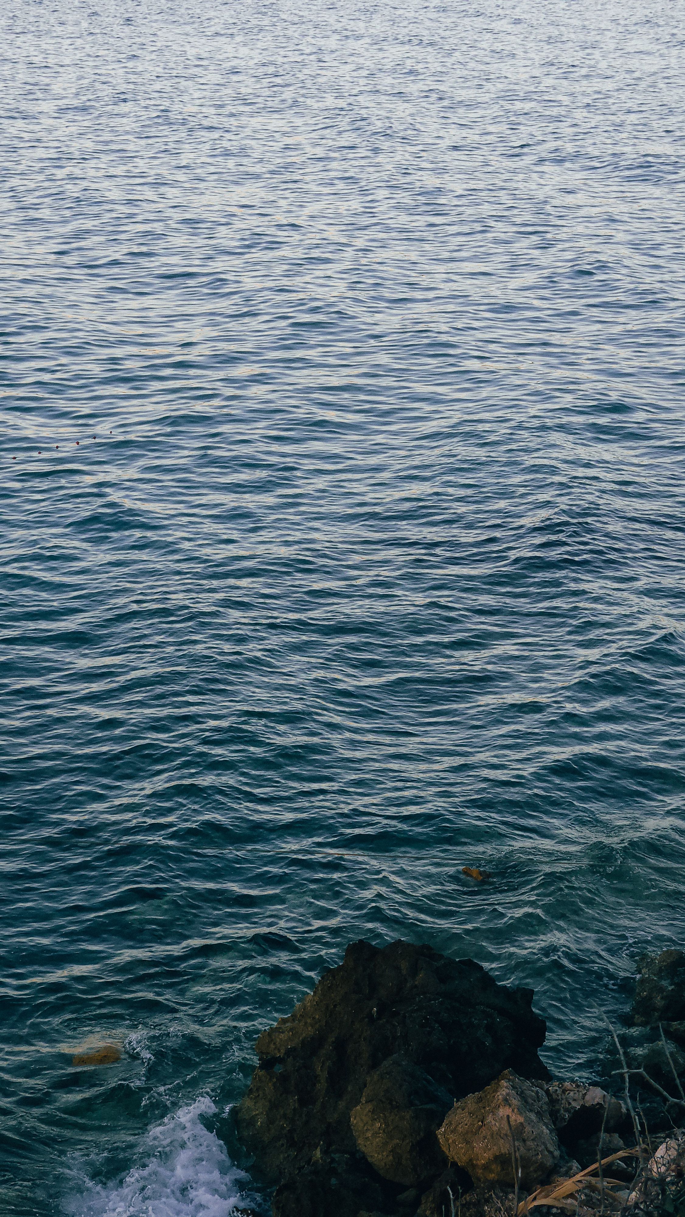 A photo of the ocean with a person standing on the rocks · Free Stock Photo