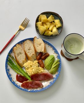 An appetizing breakfast with bread, avocado, asparagus, pineapple, and a hot drink.