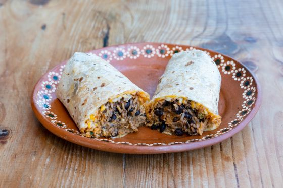 Two burrito halves stuffed with black beans, rice and melted cheese on a clay plate