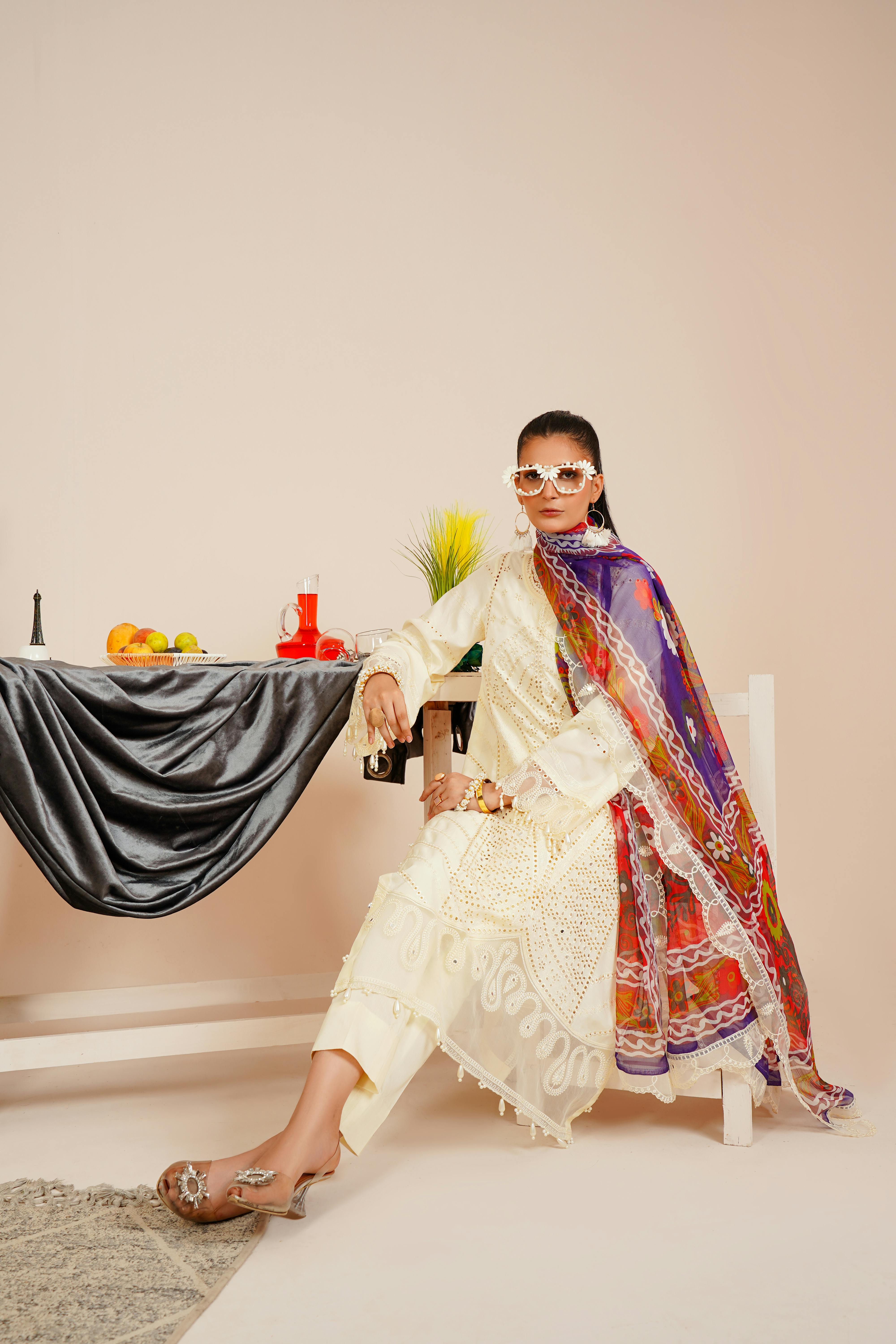 A fashionable young woman in traditional Pakistani attire, seated indoors.