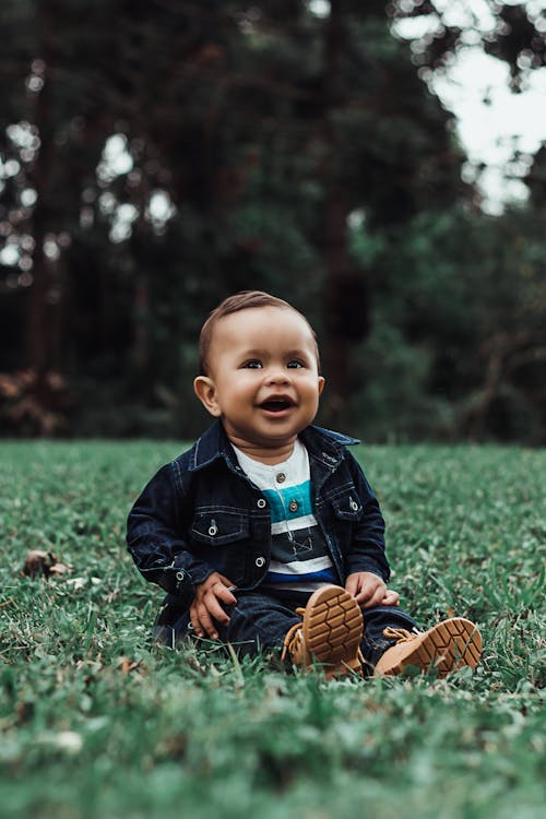 Free Photo of Smiling Baby Boy in Denim Outfit Sitting on Grass Stock Photo
