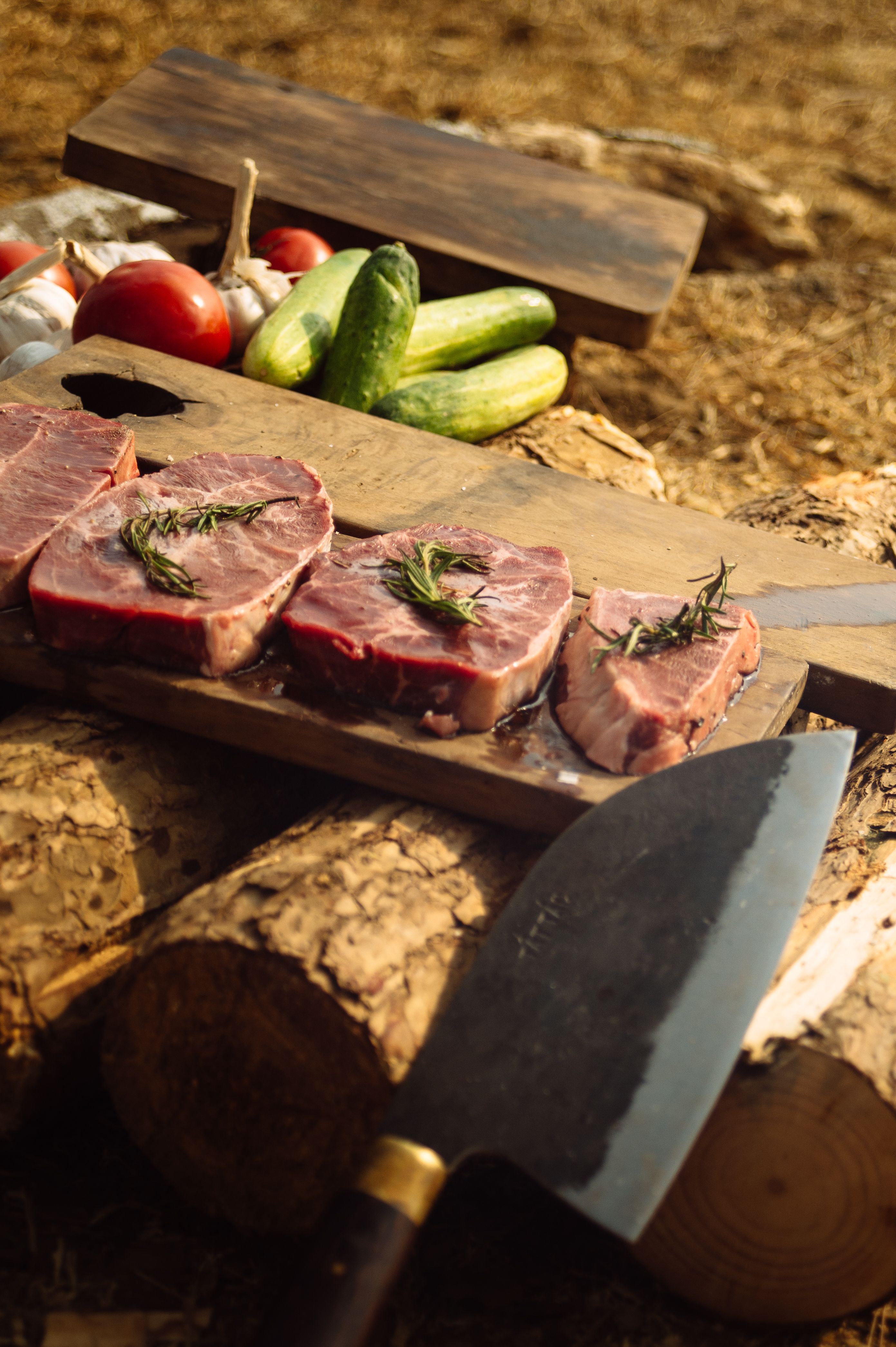 Sliced meat on a wooden board with vegetables, ready for cooking outdoors.