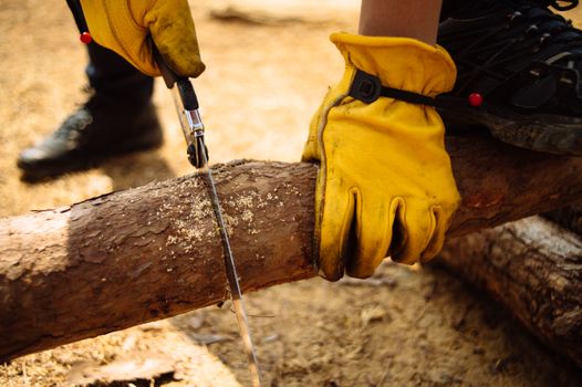 Person sawing wood outdoors with yellow gloves for safety, showcasing woodworking skills.