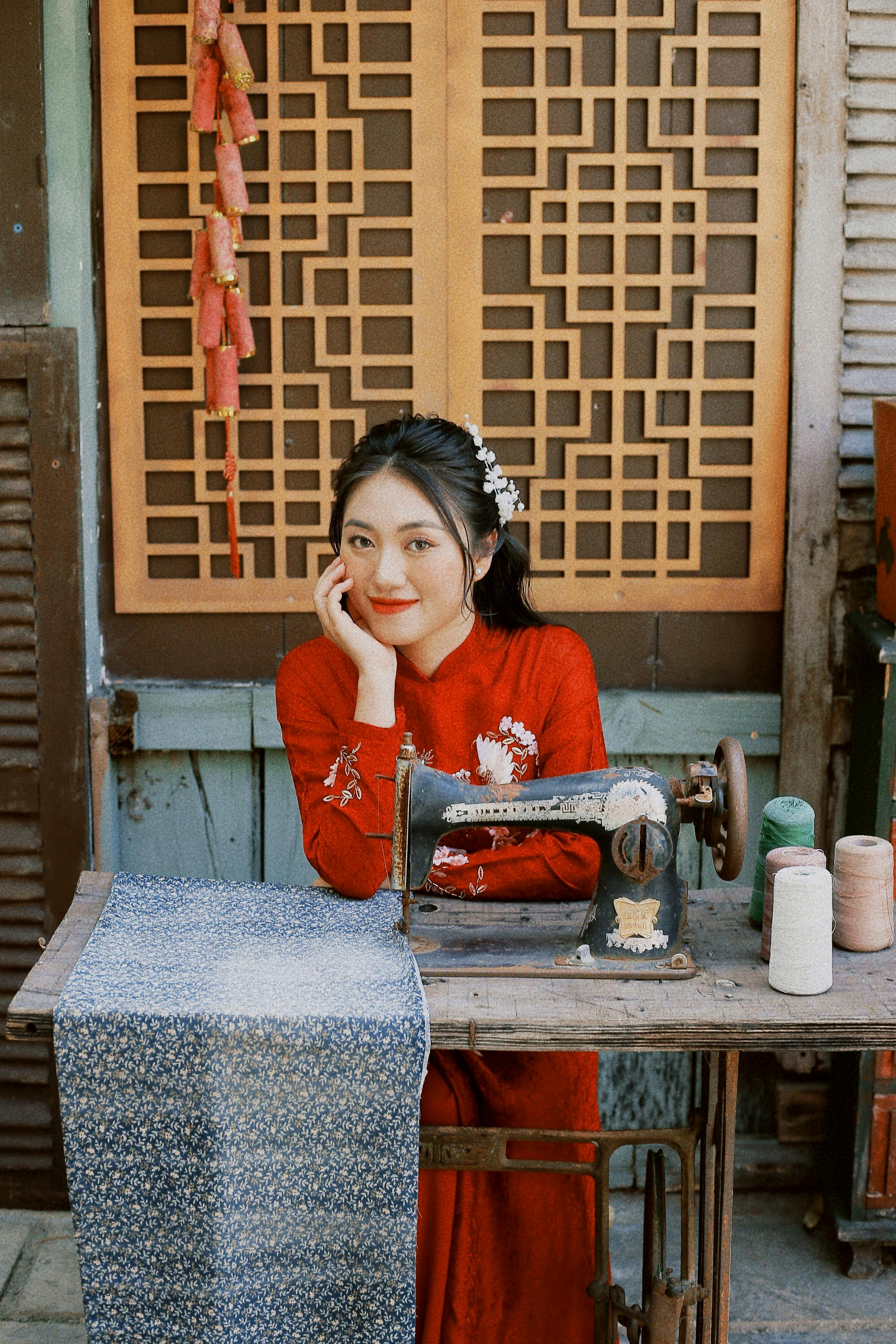 Woman in red dress posing with a vintage sewing machine in a traditional setting.
