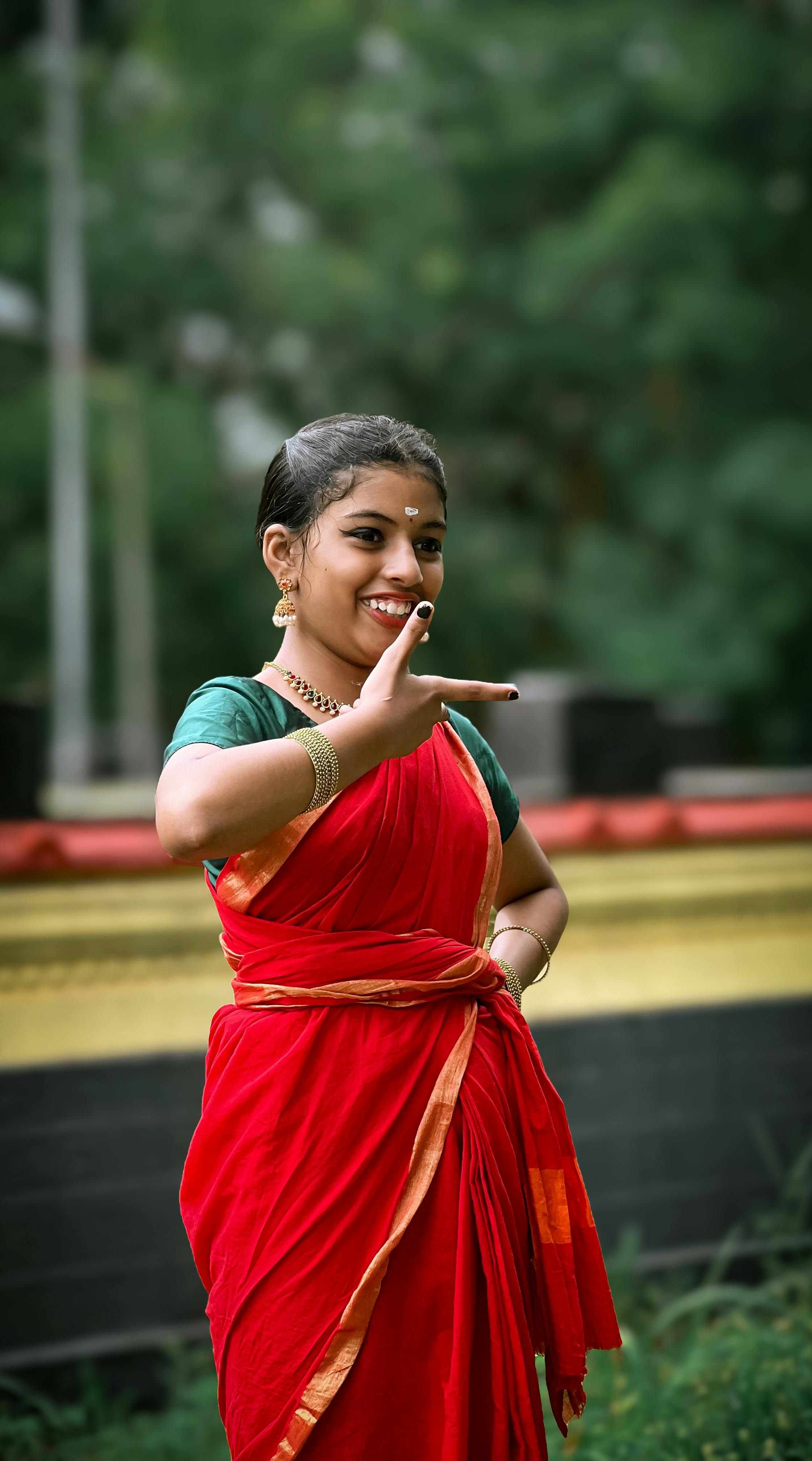 A young woman performs a traditional dance in a vibrant red sari in an outdoor setting.