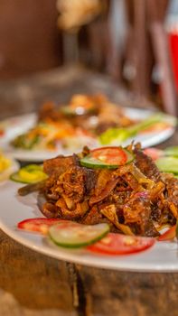 Mouth-watering beef dish with sliced vegetables on a white plate indoors.