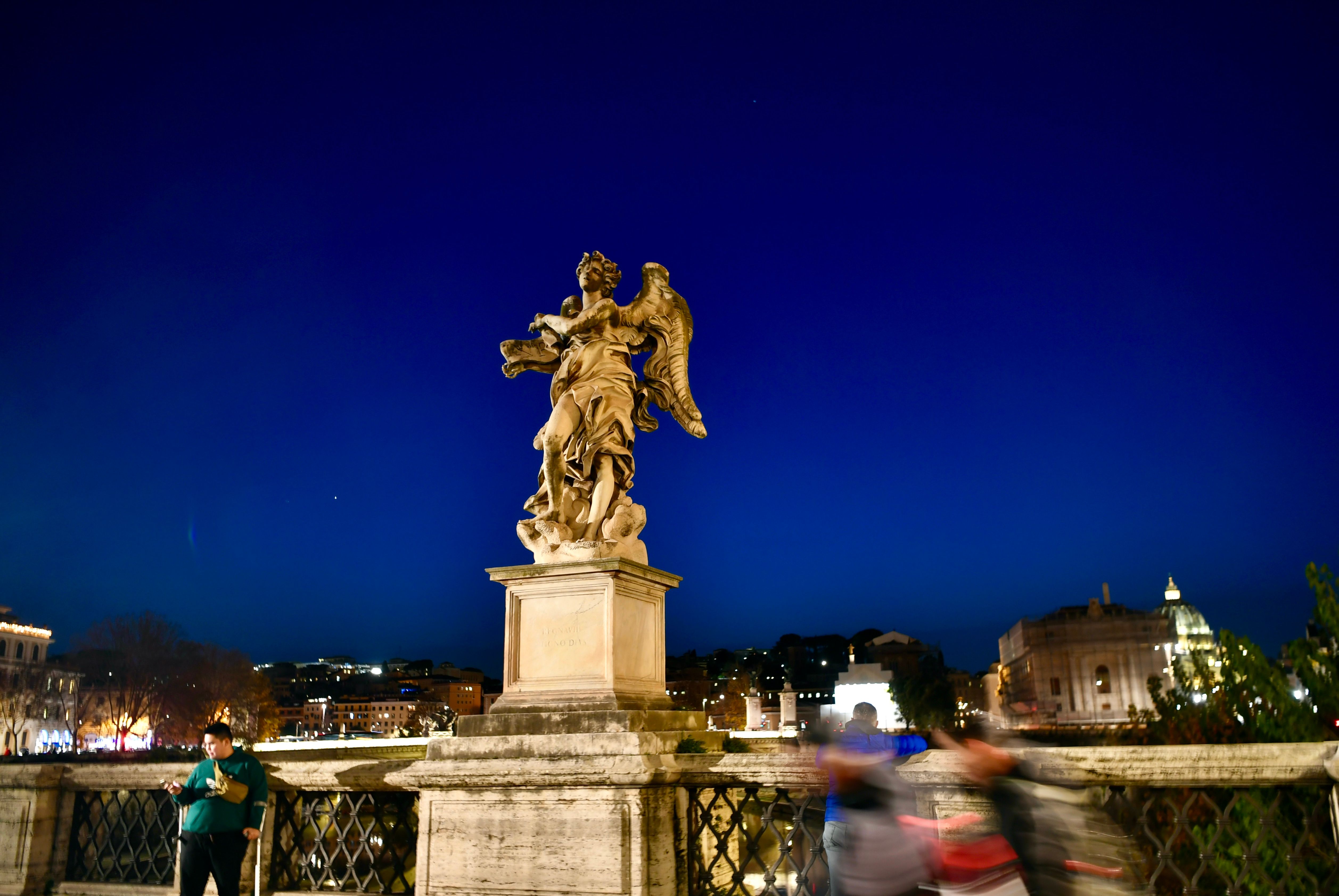 A statue of an angel on a bridge at night · Free Stock Photo