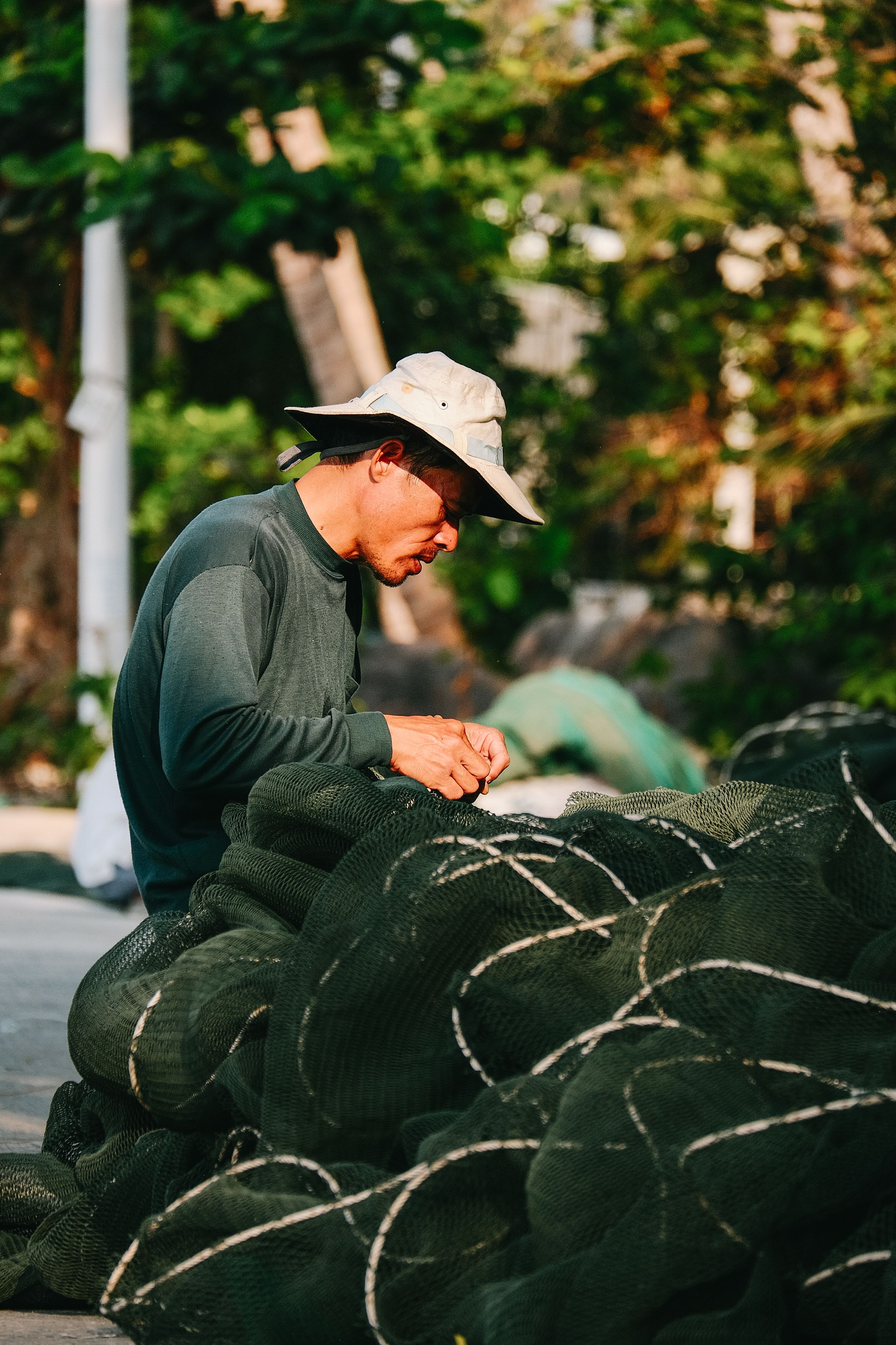 A focused Vietnamese fisherman working on a fishing net outdoors in Rạch Giá, Vietnam.