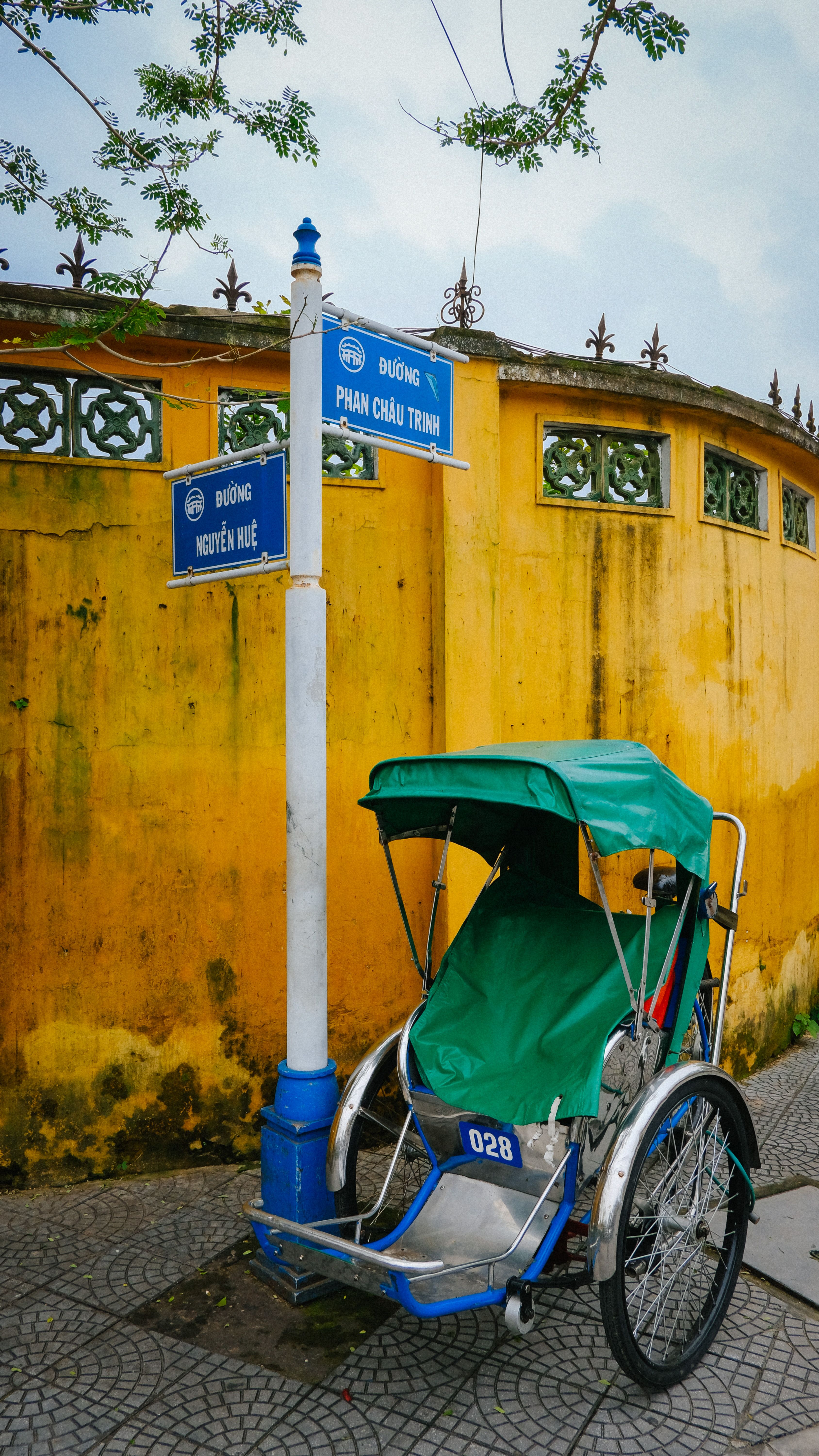 A traditional Vietnamese rickshaw parked by a yellow wall with street signs in Hội An.
