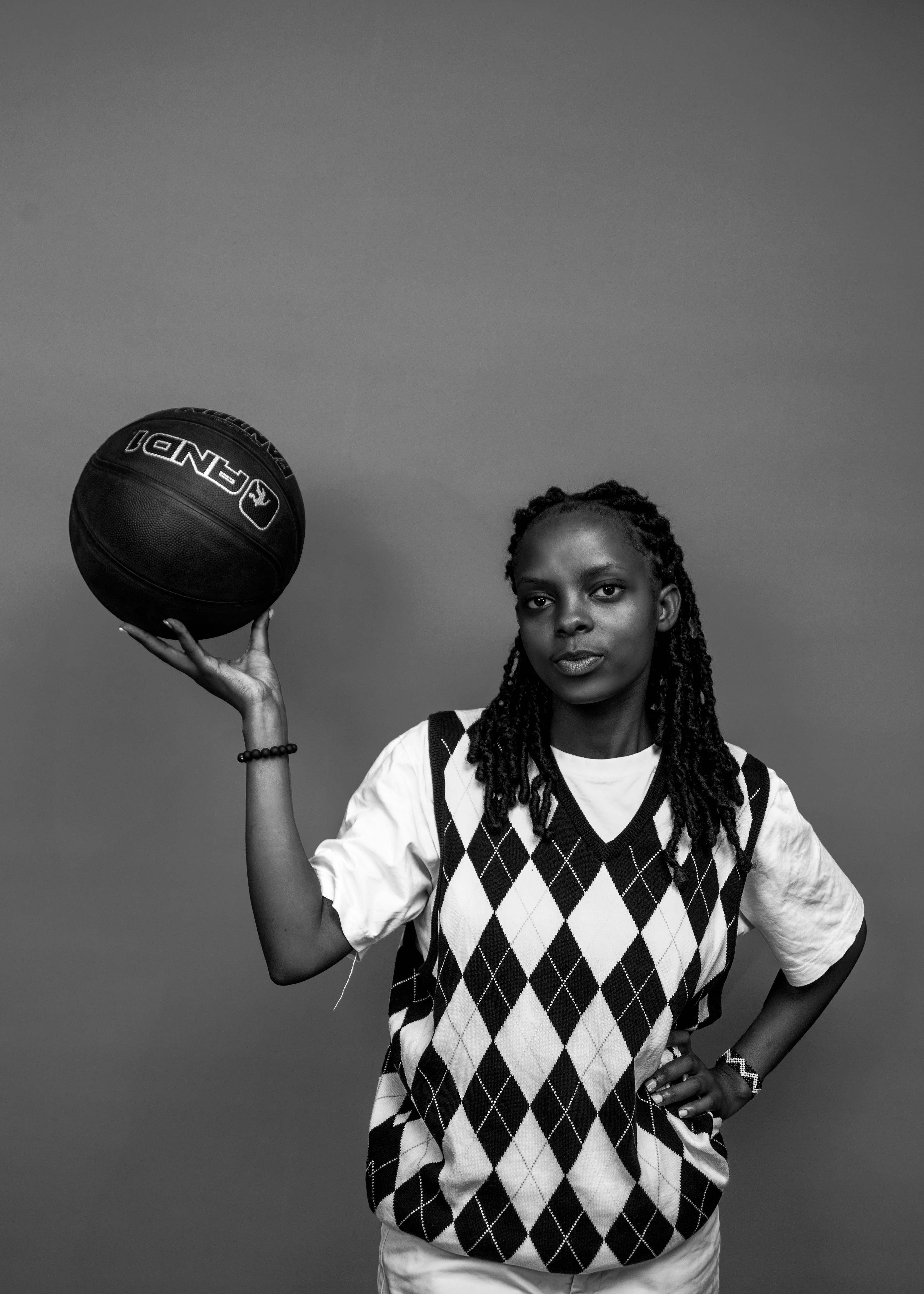 Black and white portrait of a young woman with dreadlocks holding a basketball in Kigali studio.