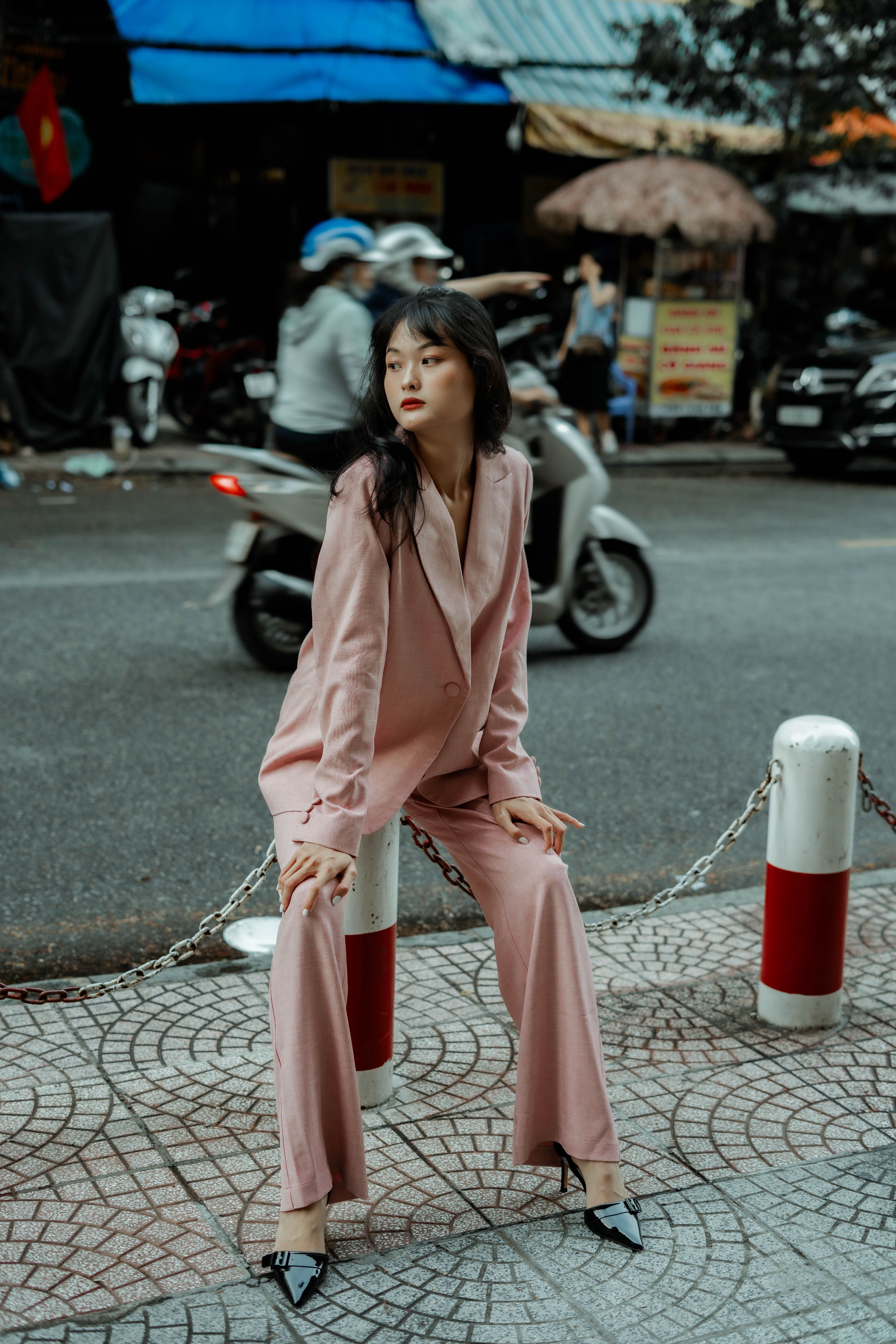 Stylish woman in a pink suit poses confidently on an urban street with motion blur from passing vehicles.