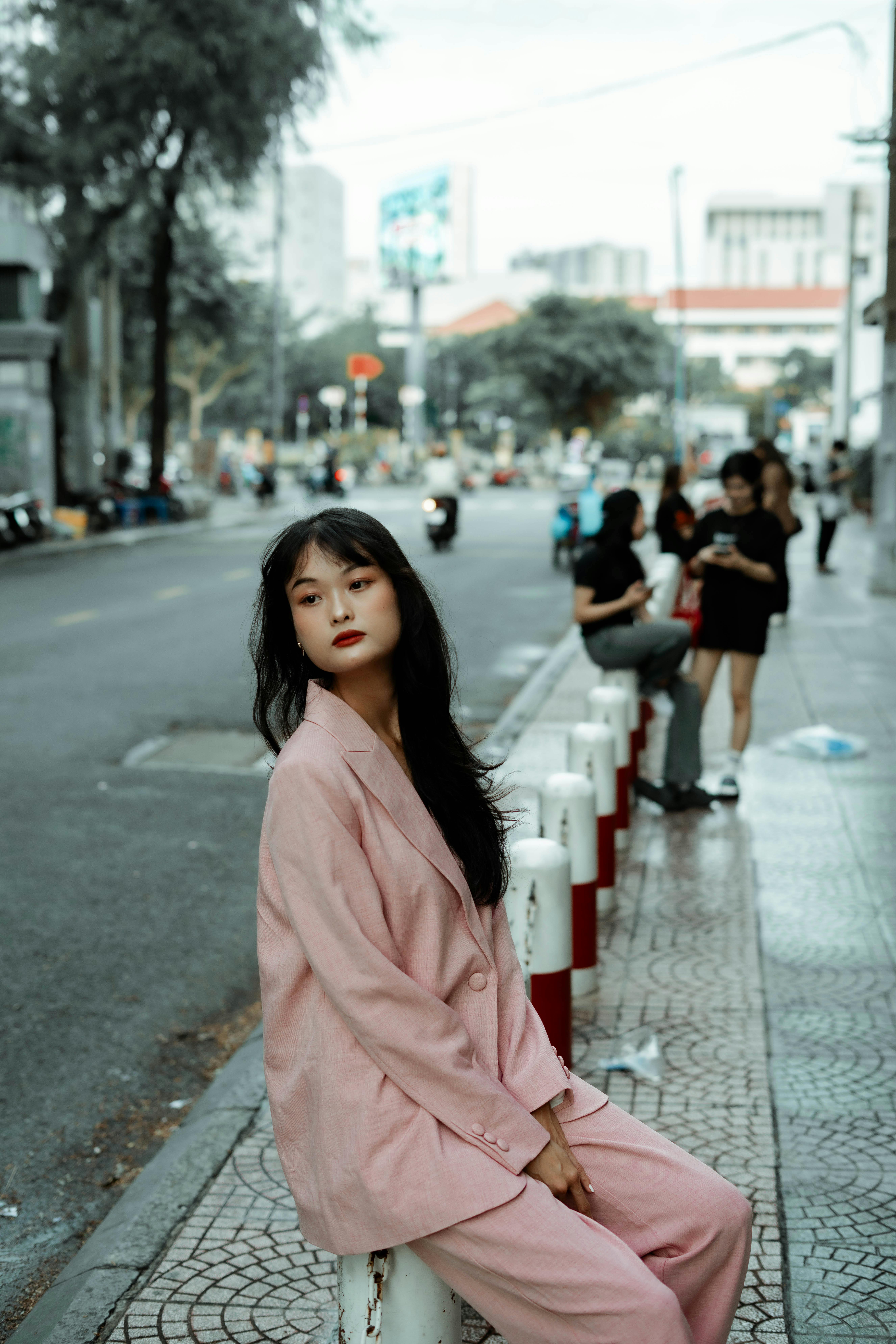 Elegant woman in a pink suit sitting on an urban street, showcasing fashion amidst the city backdrop.