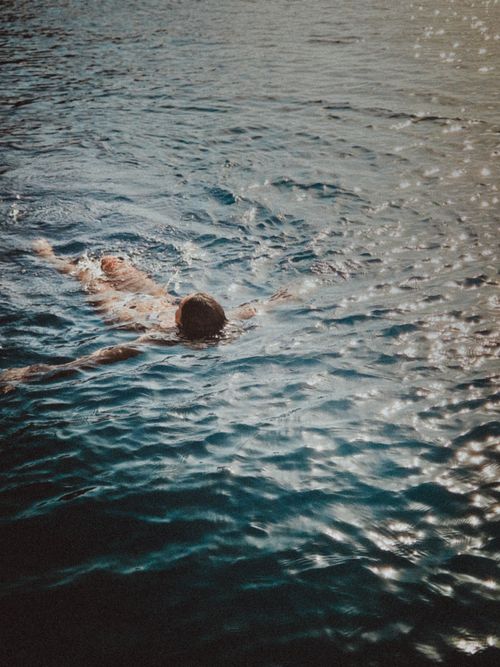 Free A man enjoying a swim in the sunlit ocean, creating ripples as he moves. Stock Photo
