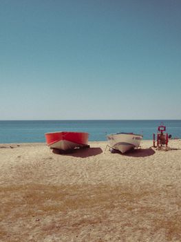 Quiet beach scene with two boats and a lifeguard chair under a clear blue sky.