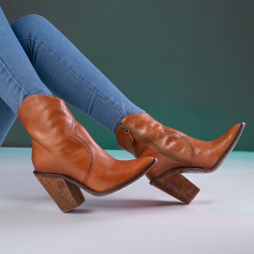 Free Chic display of brown leather boots paired with denim jeans against a green background. Stock Photo