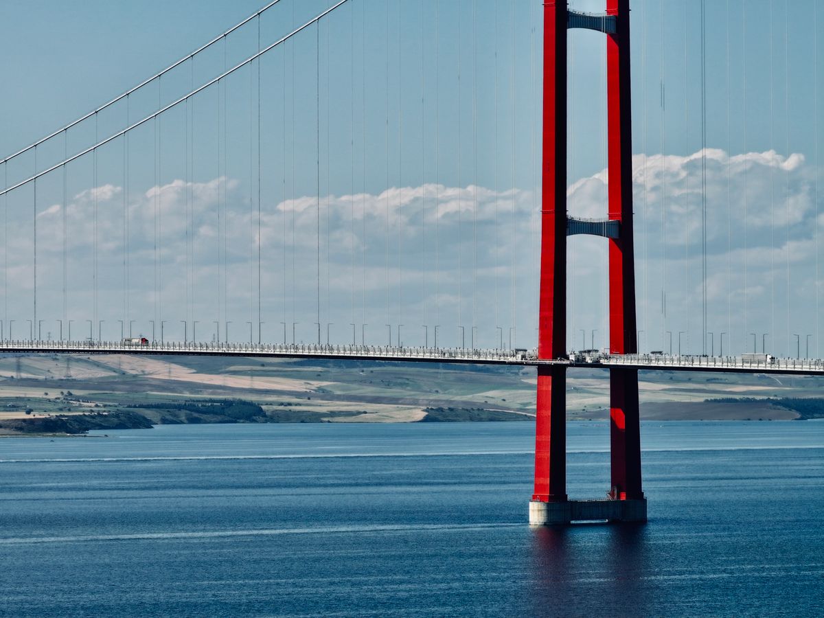 A red suspension bridge towering over bright blue ocean waters between islands