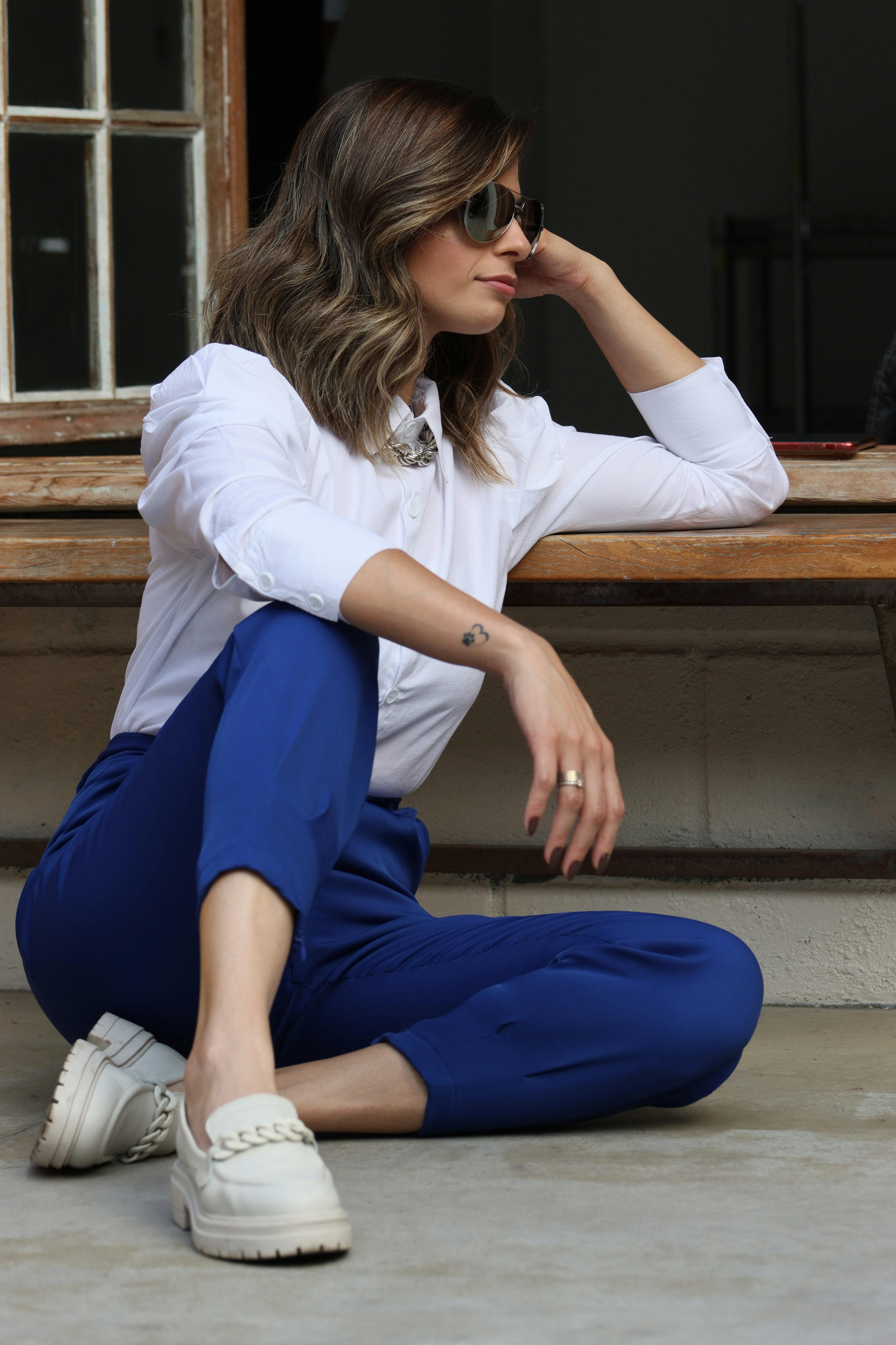 A woman sitting on the ground wearing blue pants and white shirt