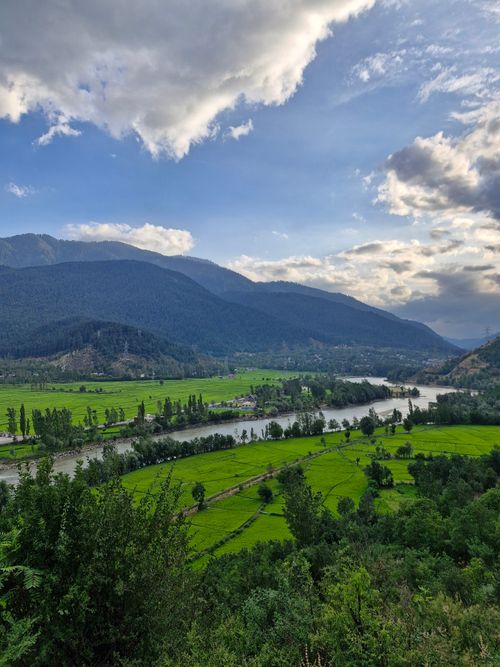 Free Beautiful summer landscape featuring a lush green valley nestled between mountains with a winding river under a partly cloudy sky. Stock Photo