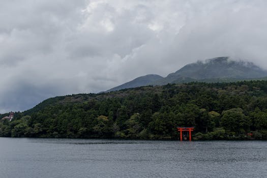 Peaceful scene of Lake Ashi with a vibrant red torii gate and misty mountains.