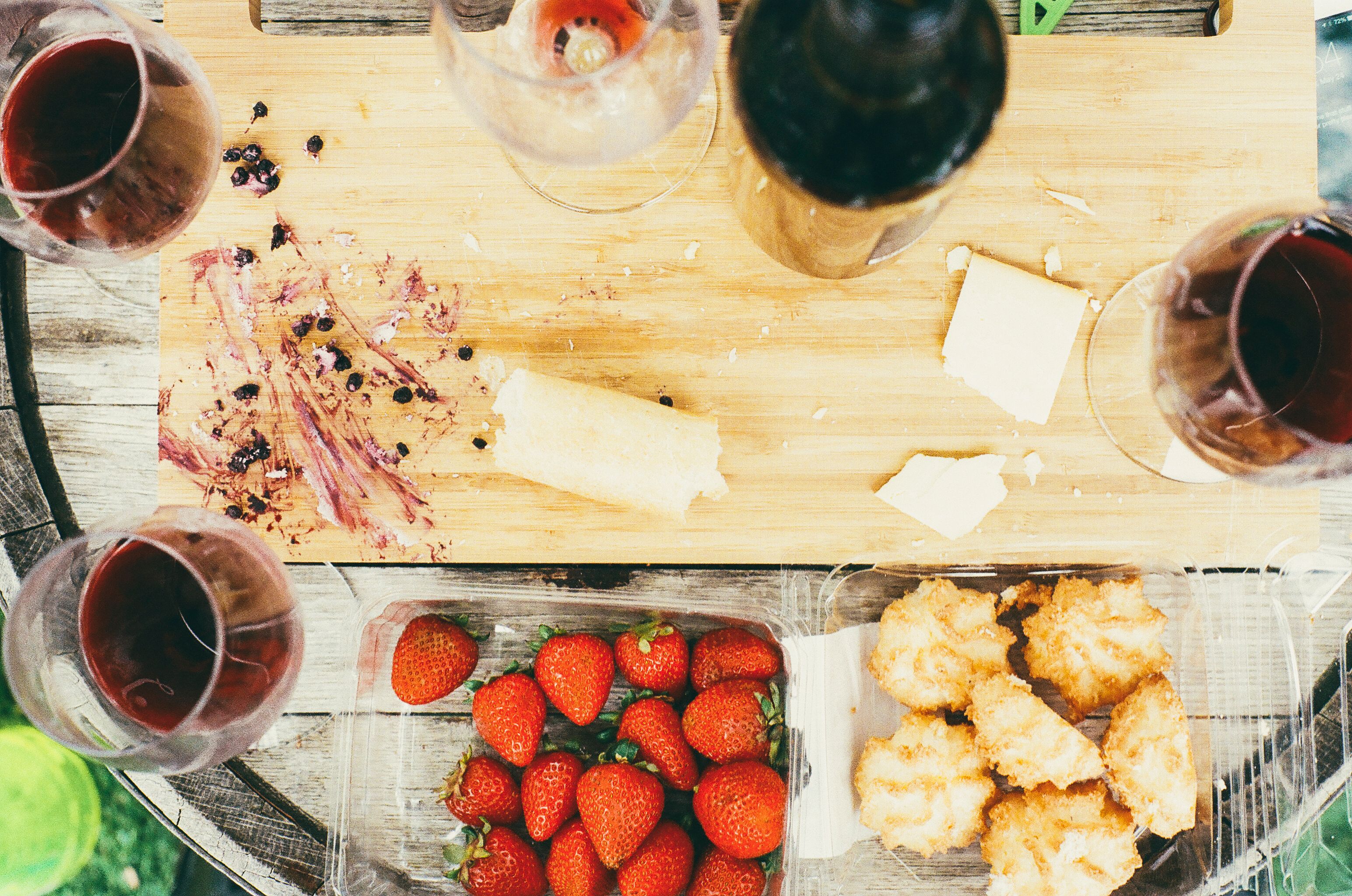 Top-down view of wine with strawberries, cheese, and pastries on a picnic table.