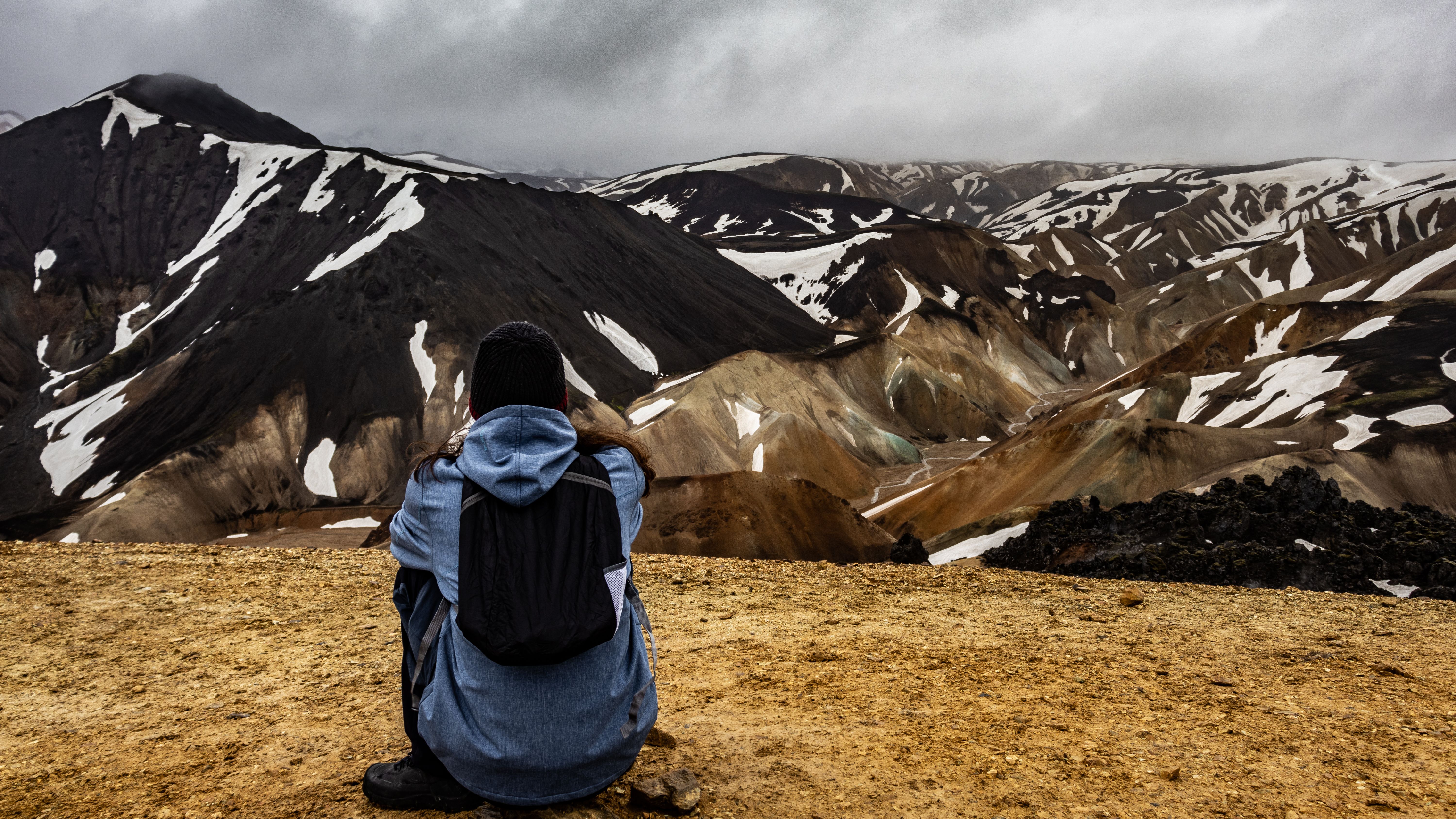 A hiker sits on a cliff overlooking Iceland's snowcapped mountains, showcasing nature's rugged beauty. A hiker sits on a cliff overlooking Iceland's snowcapped mountains, showcasing nature's rugged beauty.