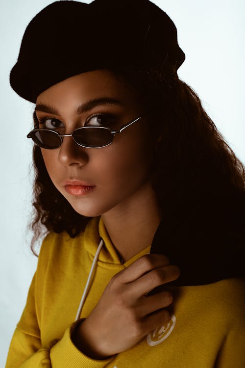 Foto De Primer Plano De Mujer Con Sombrero Boina Negra, Gafas De Sol Y Sudadera Con Capucha Amarilla Posando