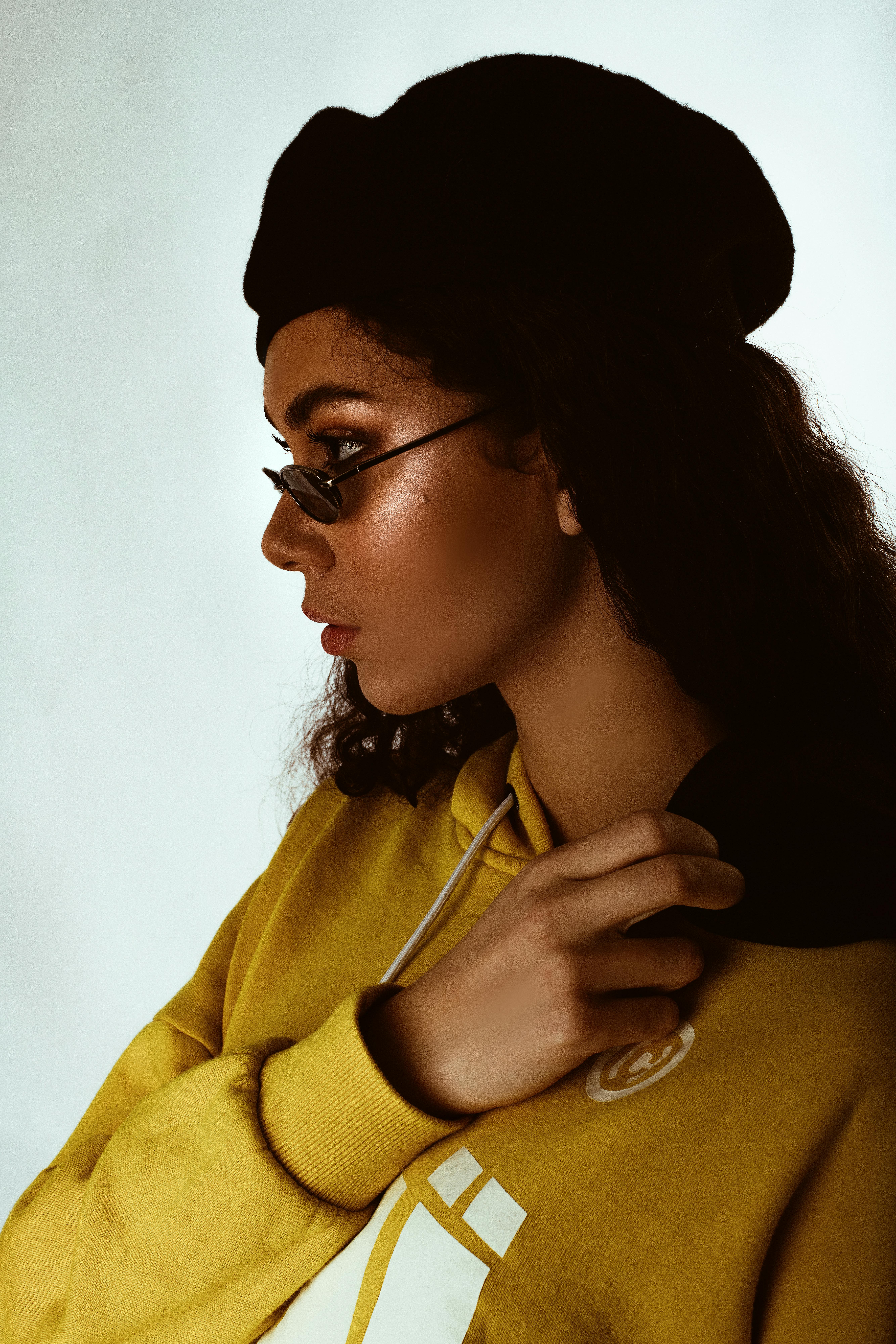 Trendy young woman wearing sunglasses, a hoodie, and a beret against a plain background.