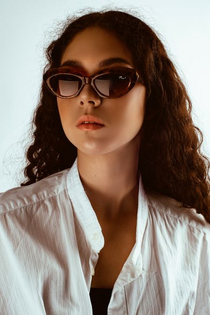 Portrait of a woman with curly hair wearing sunglasses and a white shirt.