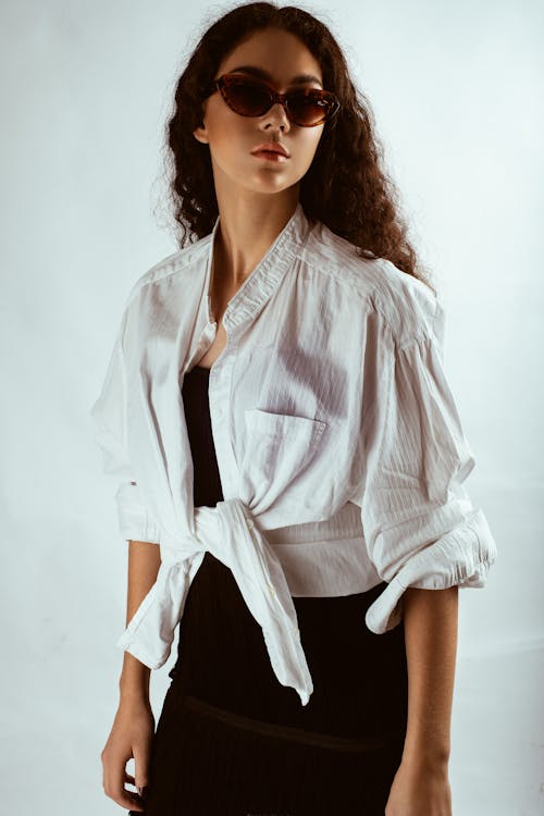 Photo of Woman in White Shirt, Black Dress, and Sunglasses Posing In Front of White Background