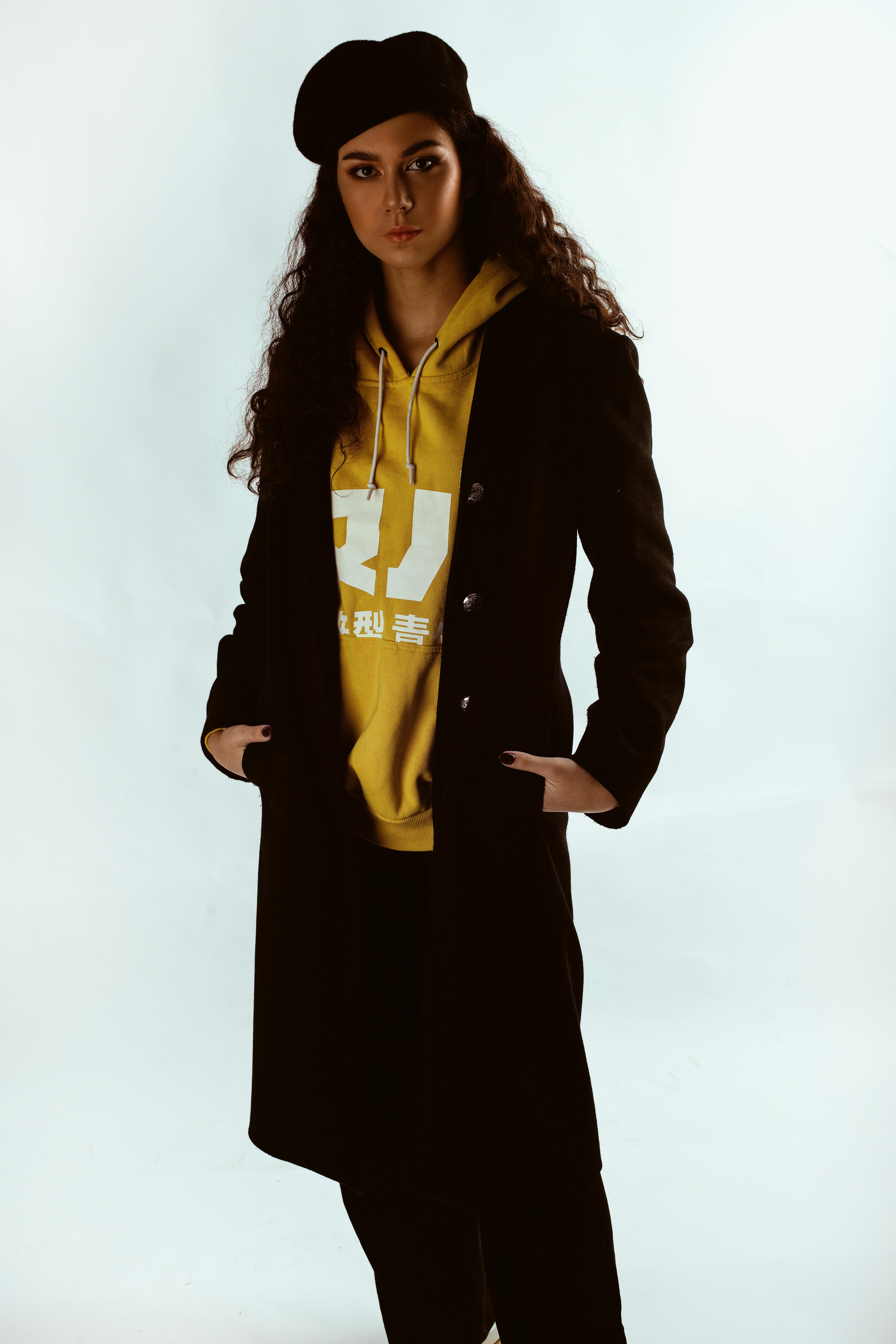 一位年轻女子穿着黑色外套和黄色连帽衫，在肖像中自信地摆出姿势