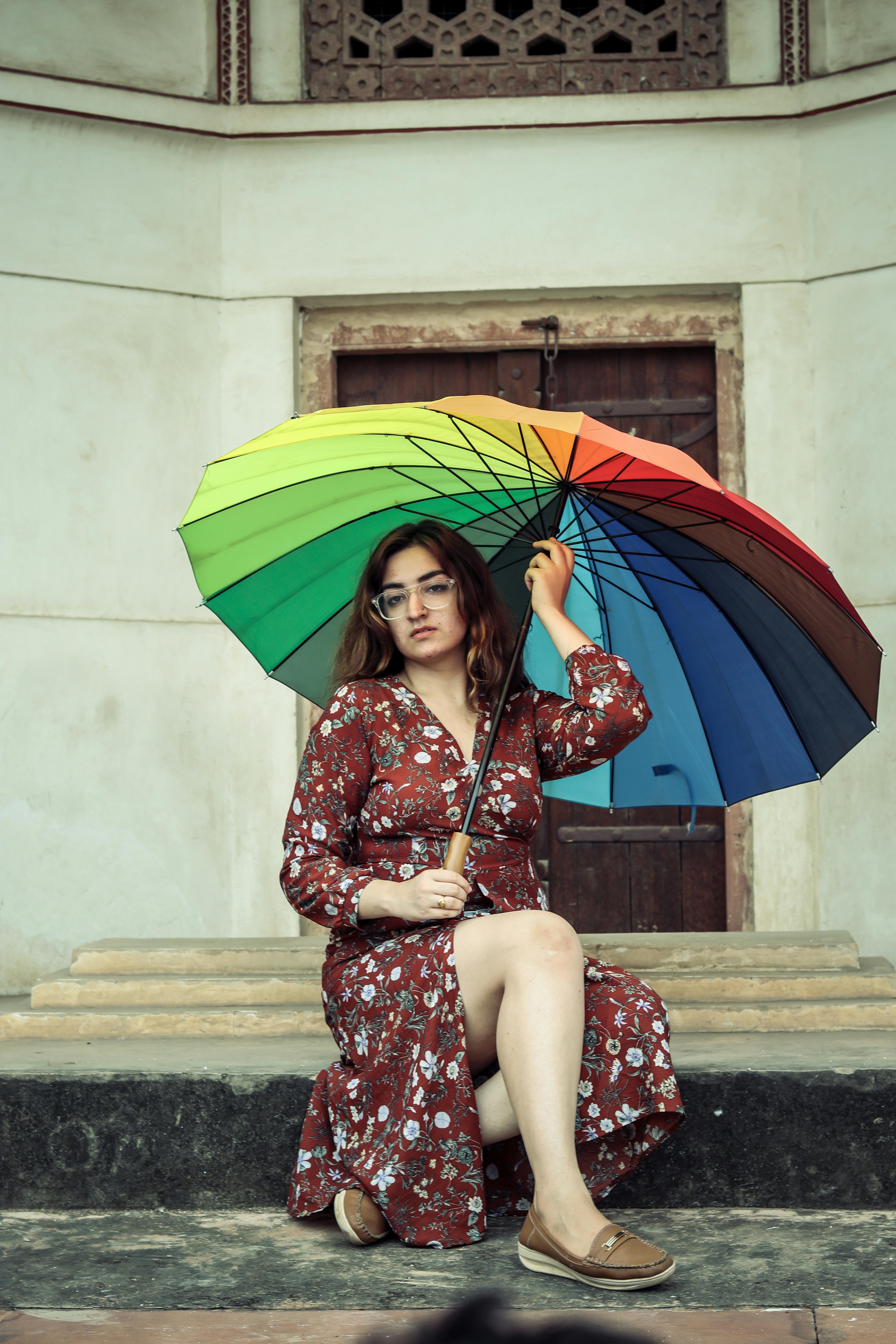 一位时尚女士穿着花卉连衣裙坐在那里，手里拿着一把充满活力的彩虹伞