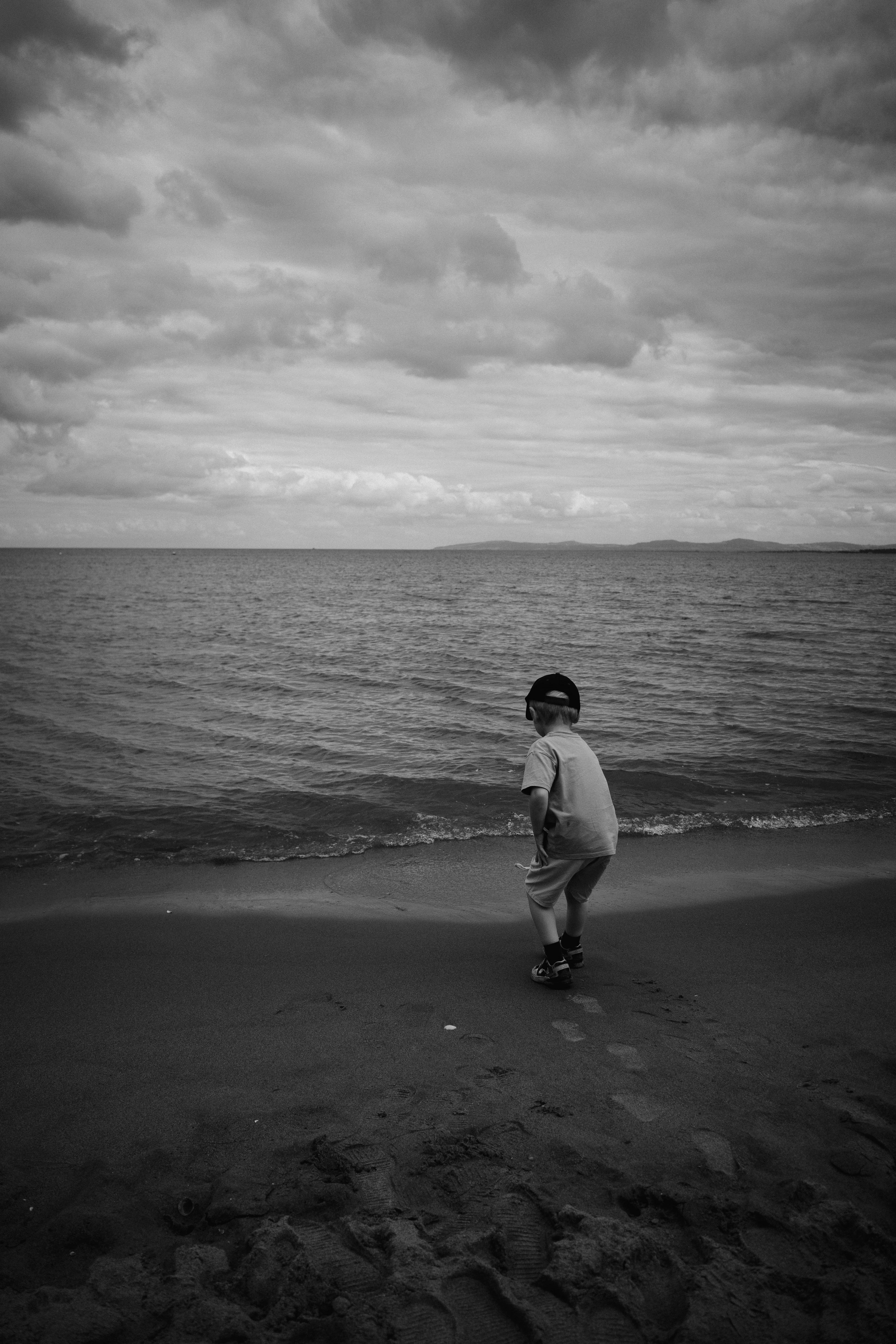 A child plays on a beach under a dramatic cloudy sky, captured in black and white.