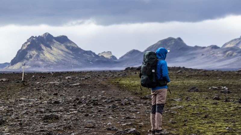Backpacker crossing a volcanic plain below jagged peaks — photo by Jędrzej Koralewski on Pexels