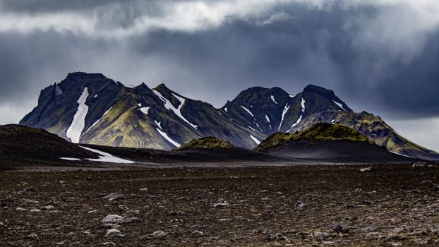 Dramatic snowy mountains under stormy skies in Iceland's rugged highlands.