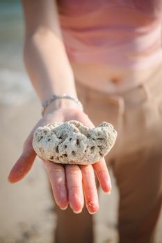 A hand holding a natural coral rock on a sunny beach, showcasing coastal beauty.